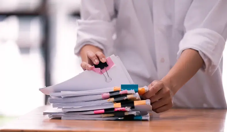 Pessoa organizando uma pilha de papéis com clips coloridos.
